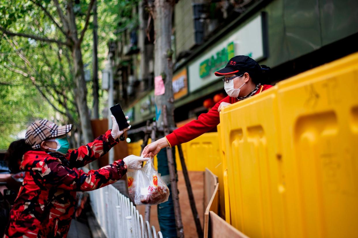 A vendor hands food to a customer over a barricade separating a residential compound in Wuhan: AFP via Getty Images