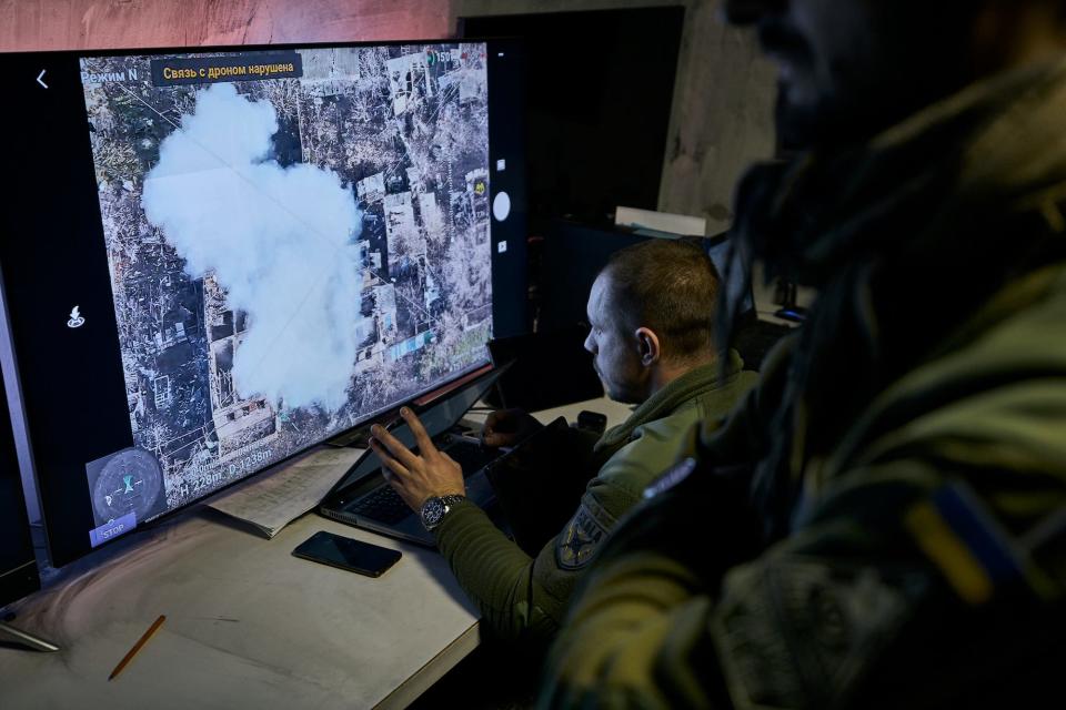 Ukrainian soldiers look at a large screen with an aerial view of Bakhmut and a plume of smoke on it