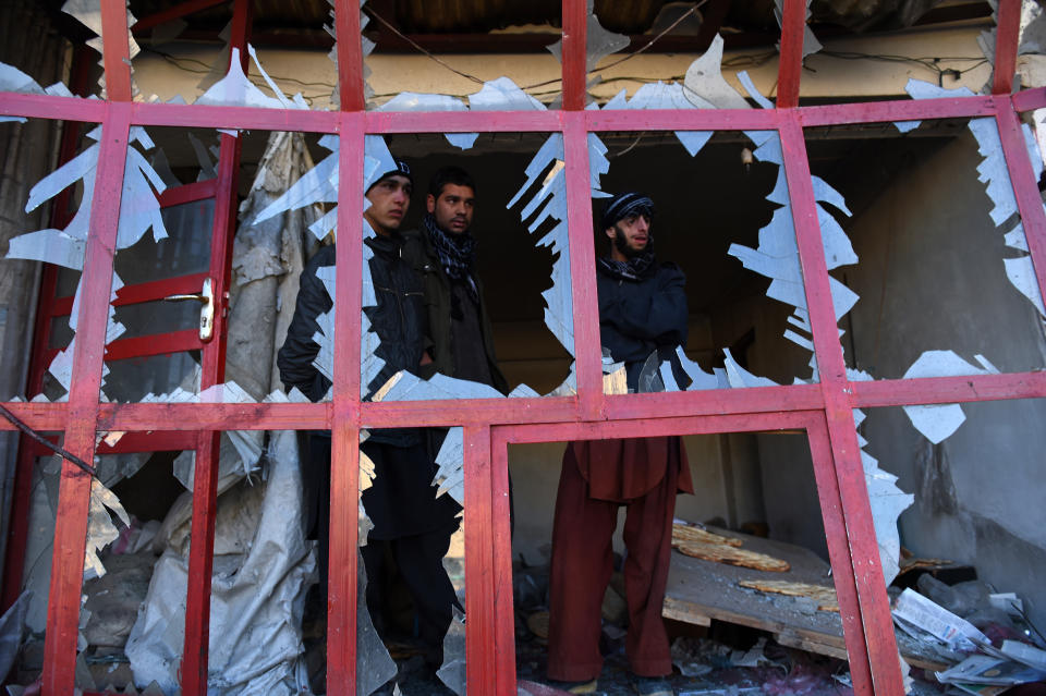 Onlookers peer through the broken windows of a bakery at the site of a suicide car bomb near the international airport in Kabul on Dec. 28, 2015.