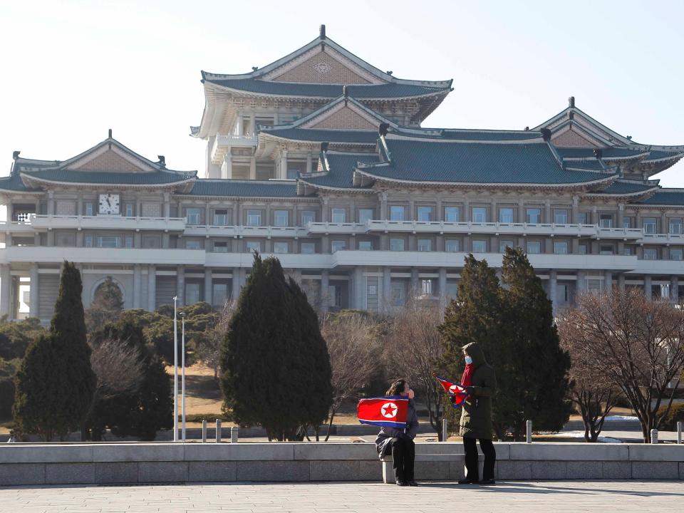 Two women sit on a chair with national flags in front of the Grand People's Study House in Pyongyang, on Thursday, Dec. 24, 2020.