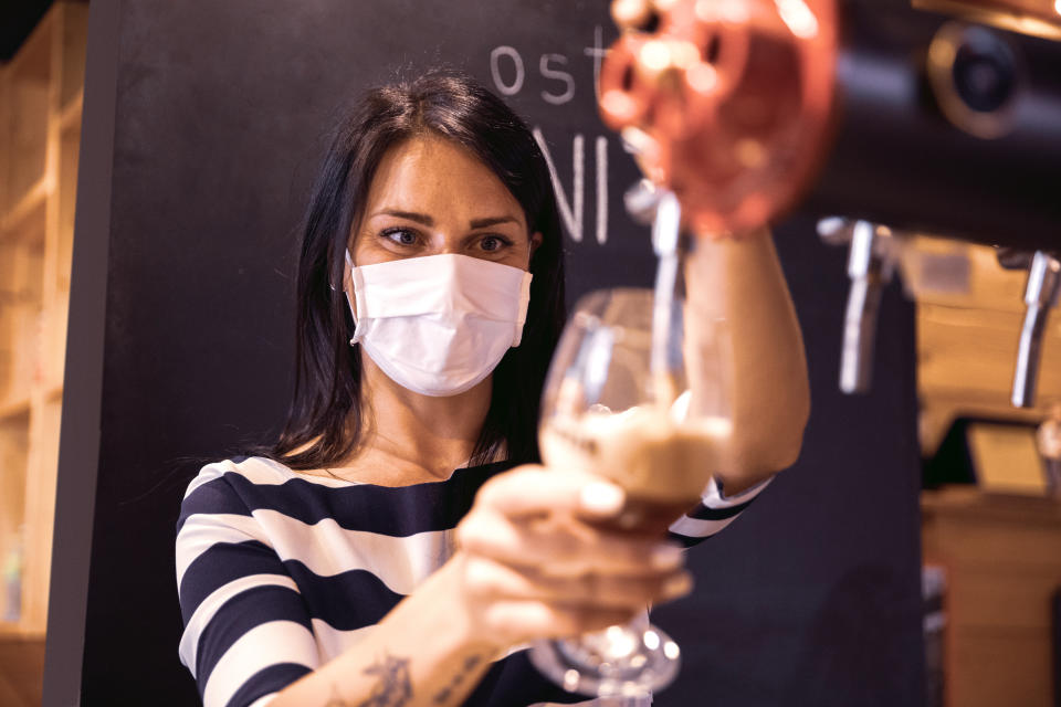 Bartender serves a fresh beer in a pub in the pandemic days, wearing protective face mask.