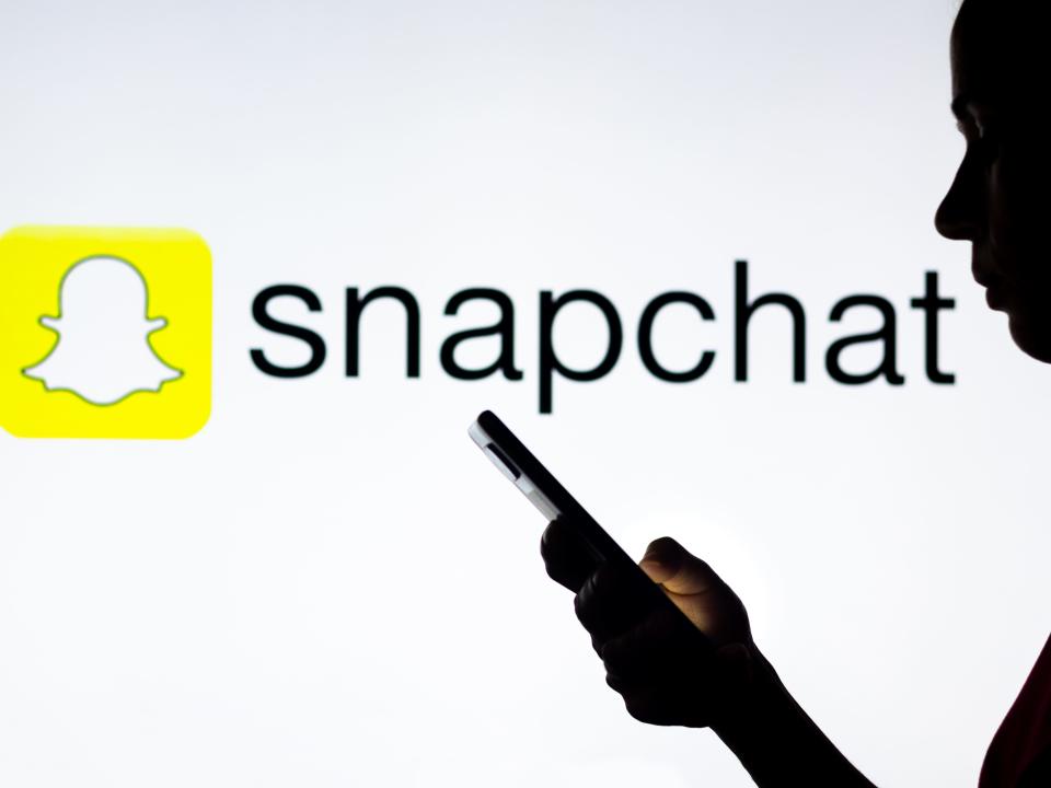 snapchat logo behind woman's silhouette holding a smartphone