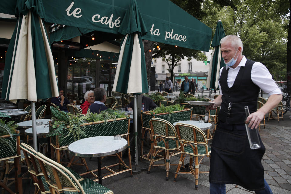 A waiter walks to serve customers at a restaurant, Monday, June 15, 2020 in Paris. Paris is rediscovering itself, as its cafes and restaurants reopen for the first time since the fast-spreading virus forced them to close their doors March 14. Restaurants outside the Paris region opened earlier this month, and Paris cafes were allowed to serve people outside but not open their doors. After three months of losses, some restaurateurs fear it will take a long time for business to come back. (AP Photo/Francois Mori)