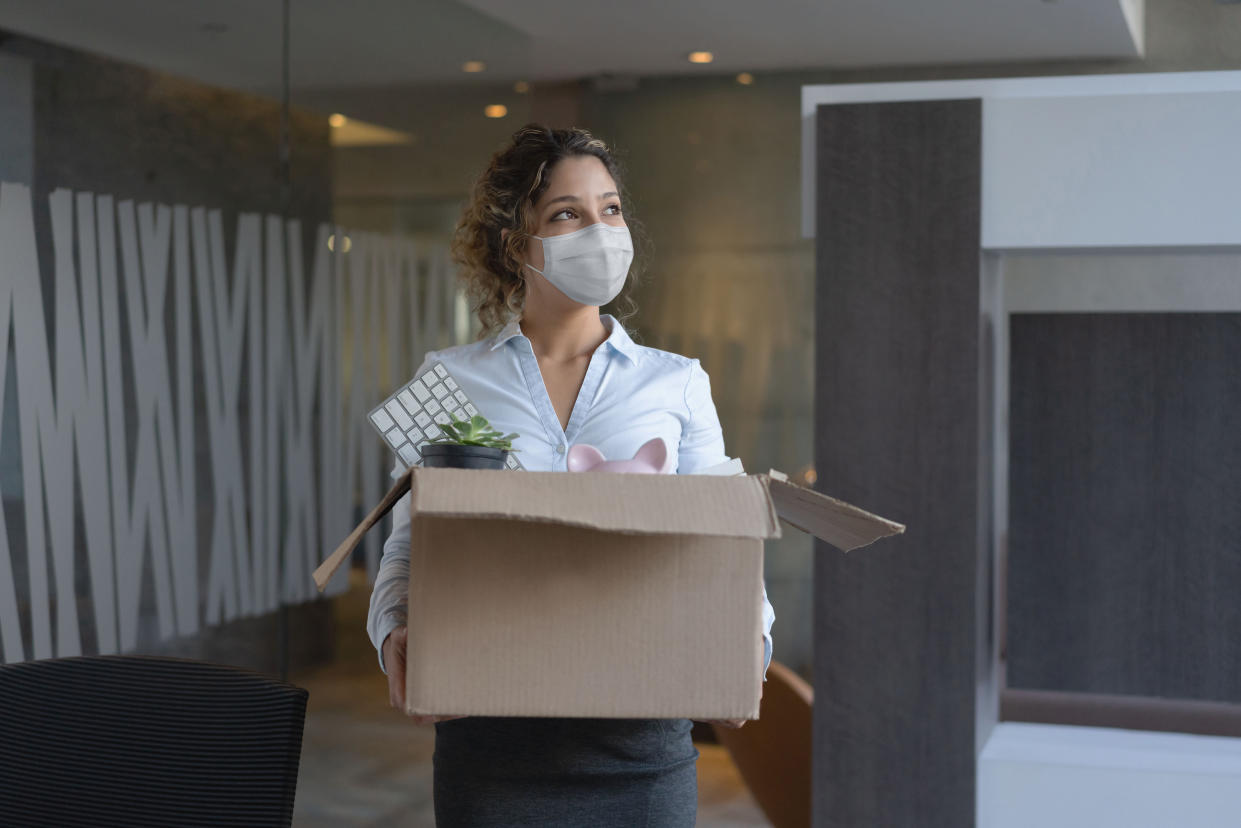 Female worker wearing a facemask at the office while holding a box with her belongings after being fired from her job during the COVID-19 pandemic