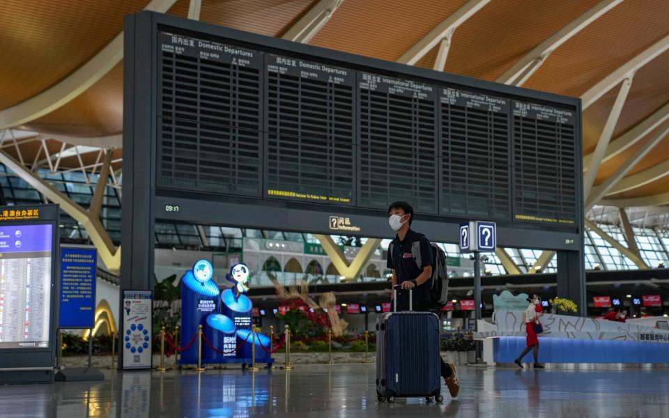 A passenger pushes his luggage past a blank flights information board at Pudong International Airport in Shanghai, China, Sunday, July 25, 2021 - AP/Andy Wong