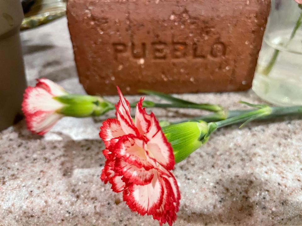 A brick embossed with the word "Pueblo" sits behind some Mother's Day carnations, May 15, 2022.