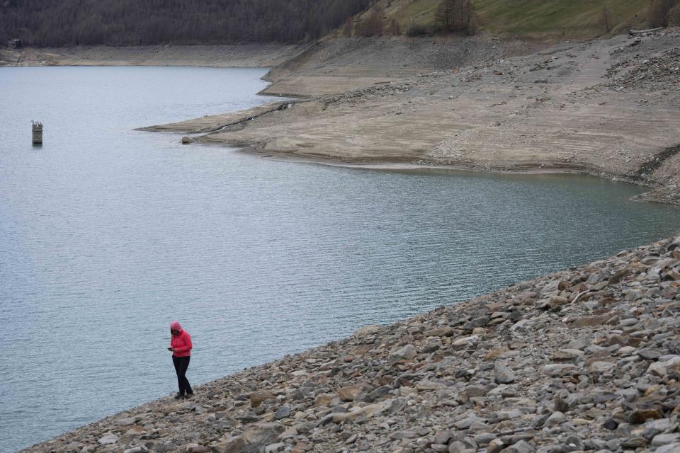 A person walks along the artificial Vernago lake, in Vernago, near the Val Senales glacier, northern Italy, Monday, April 17, 2023. The lakes are so parched an old tower is resurfacing from the bed. (AP Photo/Luca Bruno)