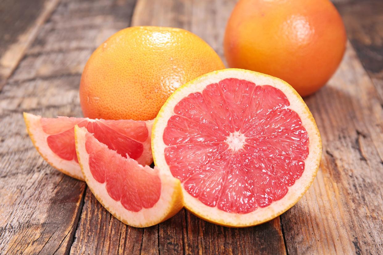 A grapefruit half with two slices next to two full grapefruits on a rustic wooden table