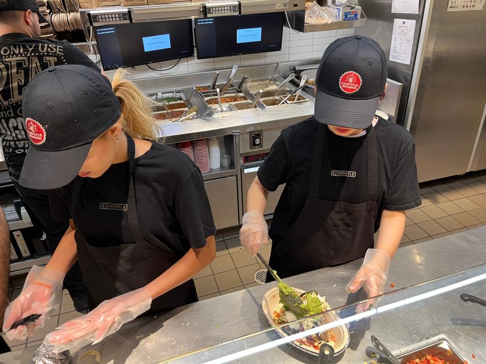 two chipotle workers making food behind the counter