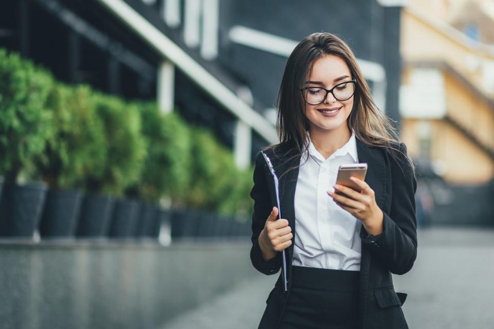 An investor is walking outside in a city and looking at something on a phone.