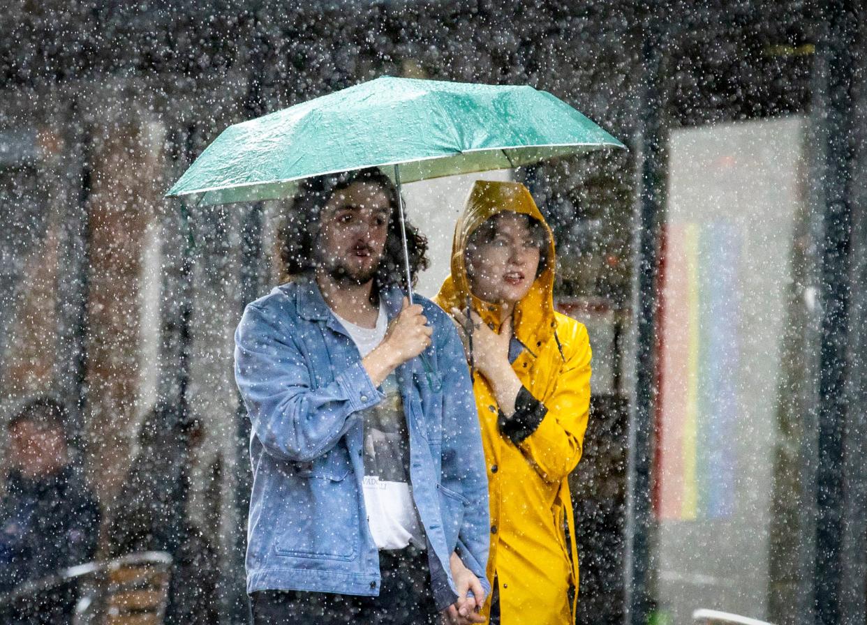A couple shelter under an umbrella during a heavy downpour of rain in Belfast, Monday 31 July (PA)