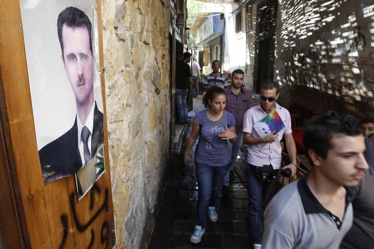People walk past a poster featuring Syrian President Bashar al-Assad in the capital Damascus on September 16, 2013