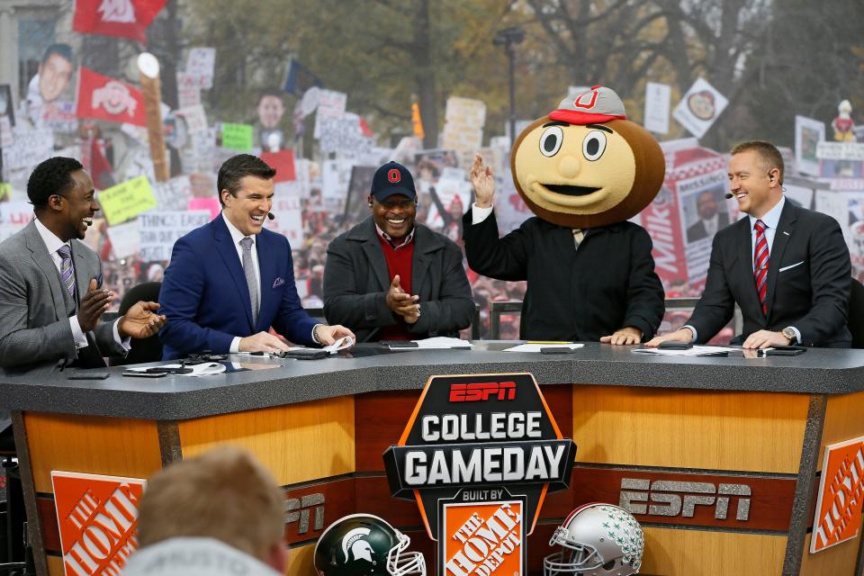 Lee Corso waves while wearing a Brutus Buckeye head as, from left, Desmond Howard, Rece Davis, Archie Griffin, and Kirk Herbstreit applaud his pick during ESPN's College GameDay broadcast from the campus of Ohio State prior to the NCAA football game against the Michigan State Spartans in Columbus on Nov. 21, 2015. (Adam Cairns / The Columbus Dispatch)