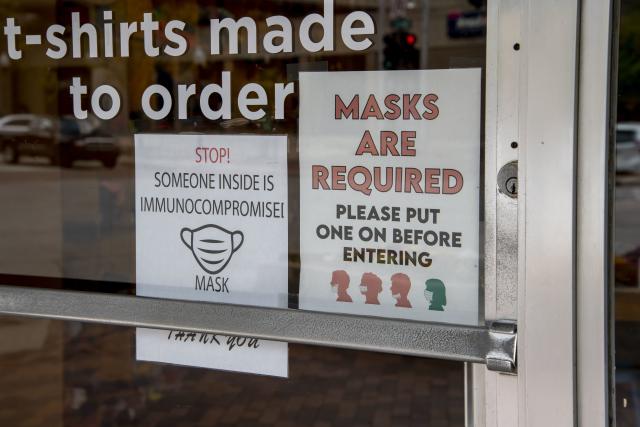 Signs in a store window read: Stop! Someone inside is immunocompromised! and Masks are required.