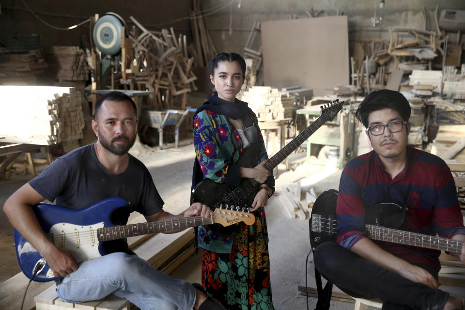 In this Thursday, July 26, 2018, photo, Afghan musicians Mohammad Rezai, right, Hakim Ebrahimi, left, and Soraya Hosseini, members of the Arikayn rock band, pose for a photo at a furniture workshop in Pakdasht, outside Tehran, Iran. The band, made up of Afghan migrants, plays Metallica-inspired ballads about the struggles of millions of Afghans who have fled to Iran to escape decades of war and unrest. (AP Photo/Ebrahim Noroozi)