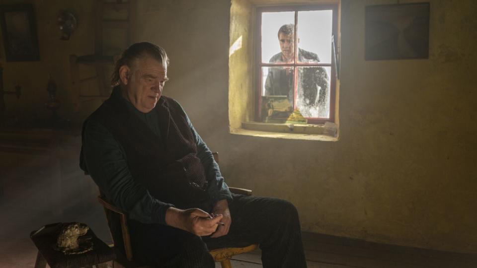 A man sits alone in his home as another man peeks in through a window.