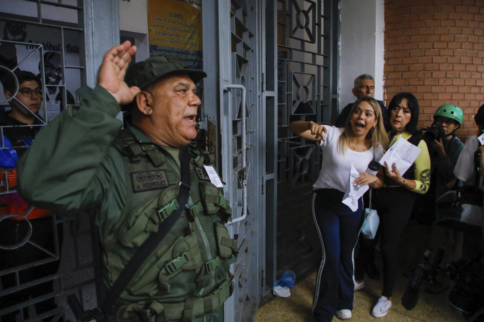 Un oficial de la Guardia Nacional se dirige a los votantes que hacen fila en la Escuela Andrés Bello mientras los observadores electorales de la oposición argumentan que no se les permite ingresar al centro de votación durante las elecciones presidenciales en Caracas, Venezuela, el domingo 28 de julio de 2024. (AP Foto/Cristian Hernández)