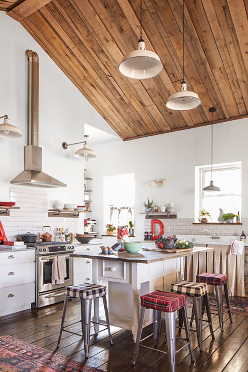 a farmhouse kitchen that is mostly white but has reclaimed lighting and an island with a wood top and barstools with plaid covers