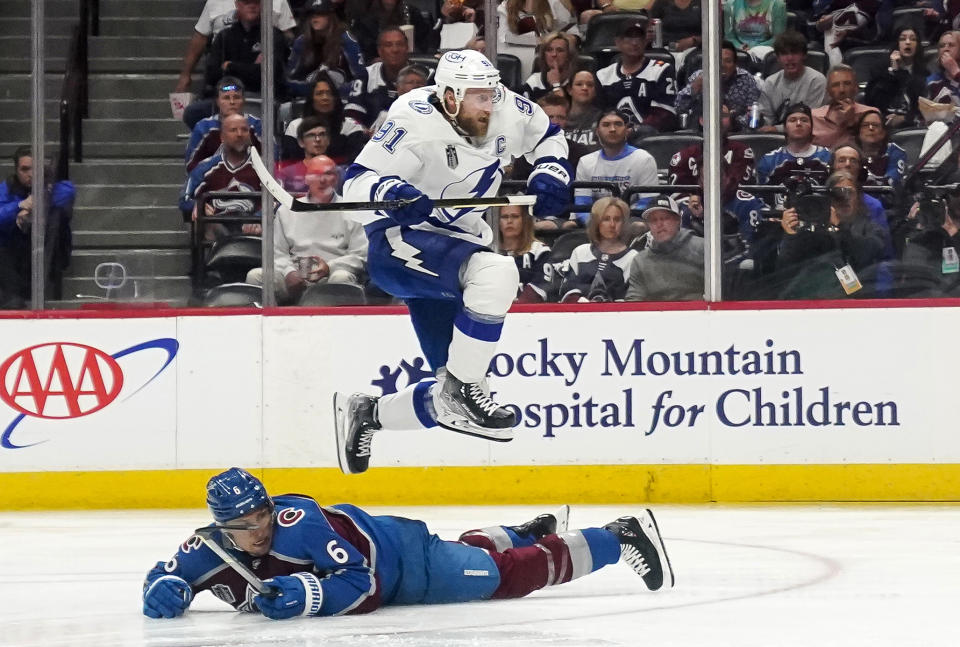 Tampa Bay Lightning center Steven Stamkos (91) jumps over Colorado Avalanche defenseman Erik Johnson (6) during the second period of Game 1 of the NHL hockey Stanley Cup Final on Wednesday, June 15, 2022, in Denver. (AP Photo/John Locher)