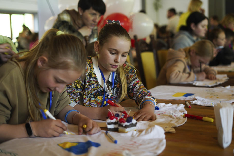 Olha Hinkina, second from left, attends an art session at the recovery camp for children and their mothers affected by the war near Lviv, Ukraine, Wednesday, May 3, 2023, as the children are given white T-shirts and instructed to express their feelings through drawing. A generation of Ukrainian children have seen their lives upended by Russia's invasion of their country. Hundreds of kids have been killed. For the survivors, the wide-ranging trauma is certain to leave psychological scars that will follow them into adolescence and adulthood. UNICEF says an estimated 1.5 million Ukrainian children are at risk of mental health issues.(AP Photo/Hanna Arhirova)