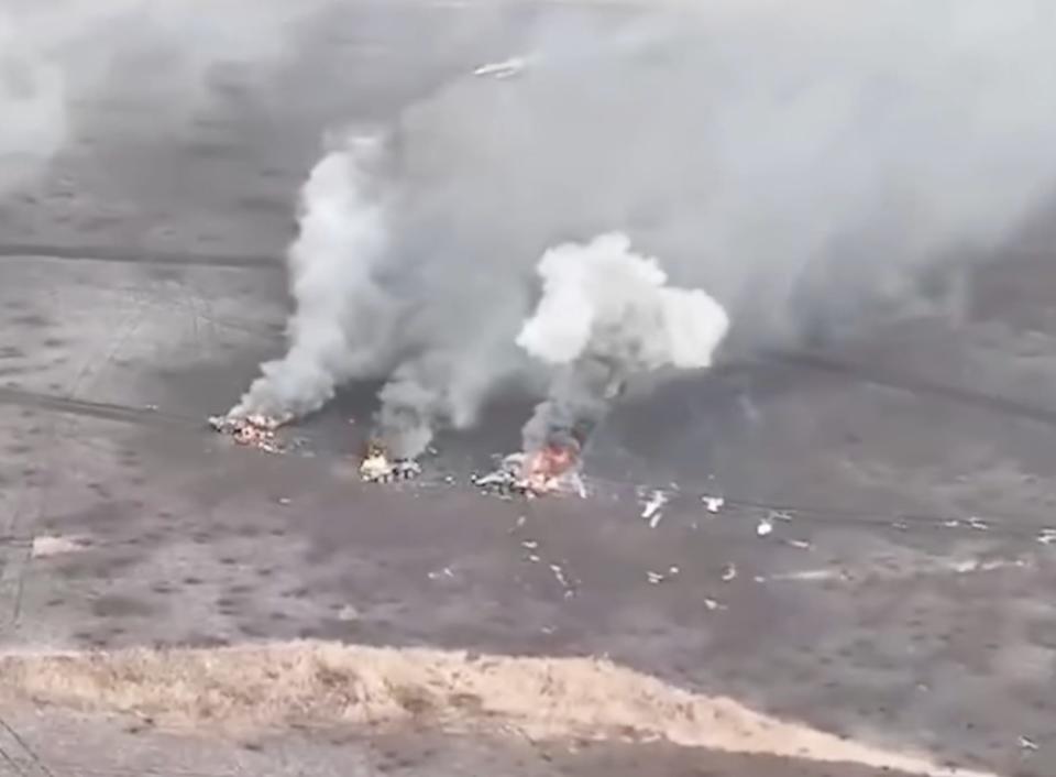 Three vehicles burning on a brown field in aerial footage