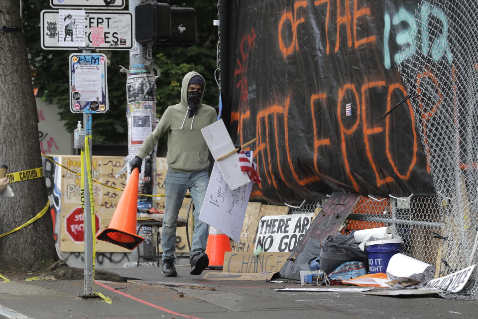 A person carries traffic cones and a U.S. flag in front of the Seattle Police East Precinct building, Saturday, June 20, 2020, inside what has been named the Capitol Hill Occupied Protest zone in Seattle. A pre-dawn shooting Saturday near the area left one person dead and critically injured another person, authorities said Saturday. The area has been occupied by protesters after Seattle Police pulled back from several blocks of the city's Capitol Hill neighborhood. (AP Photo/Ted S. Warren)