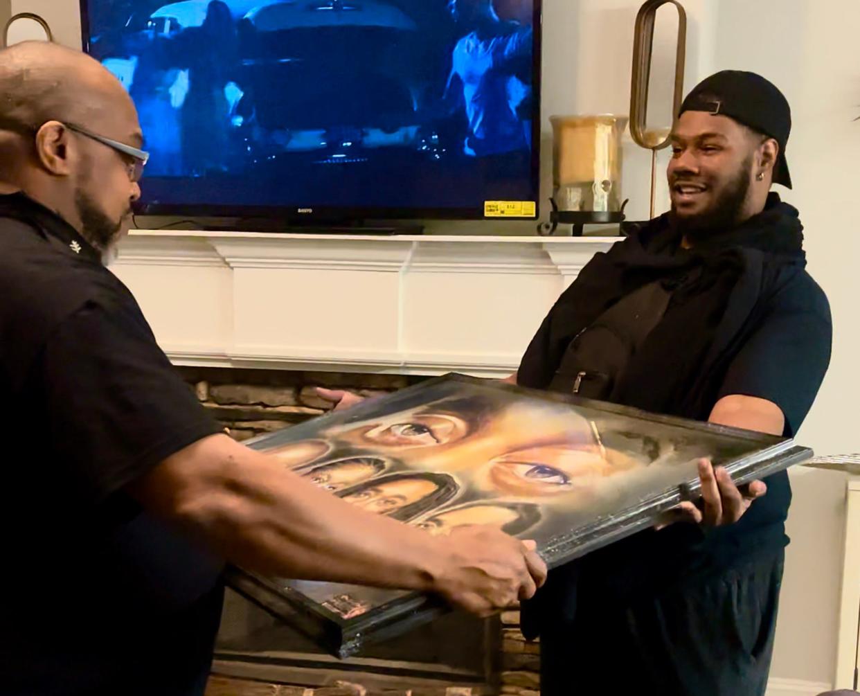 This still image taken from a video dated Nov. 16, 2022 shows (L-R) Kenneth Ball receiving a portrait of his son, Migos hip-hop group member Takeoff, from Athens artist Ronnie B. "Ron Da Don" Hull.