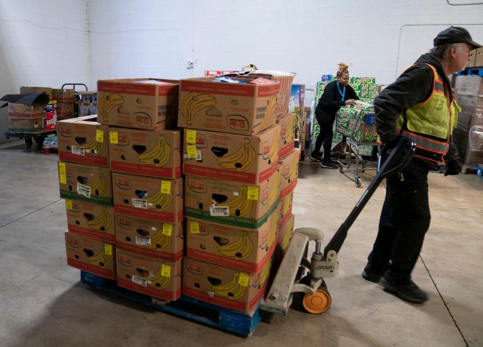 John York of Forgotten Harvest brings in a pallet of bananas as Princess Hatch, 29, fills a cart to restock the shelves at Fish and Loaves, a food pantry in Taylor on Friday, March 3, 2023.
