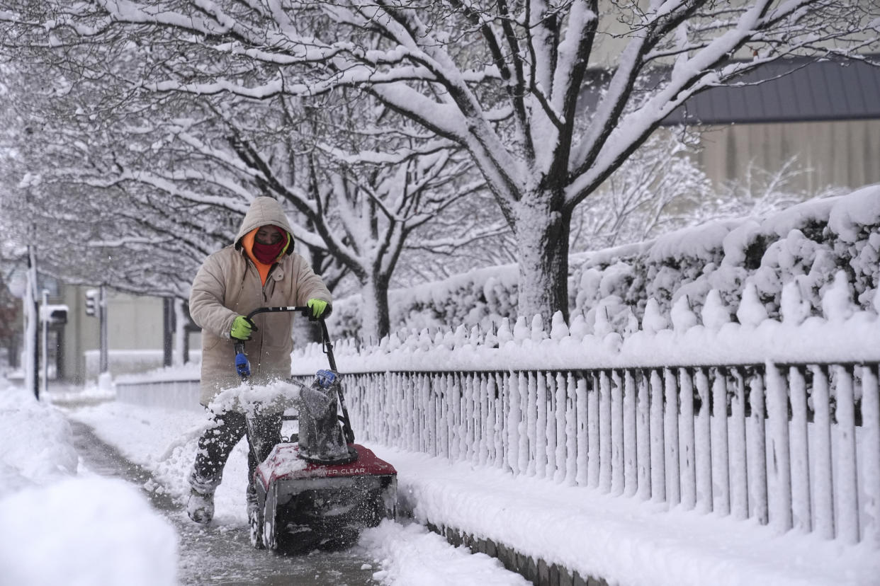 A woman clears snow off a sidewalk