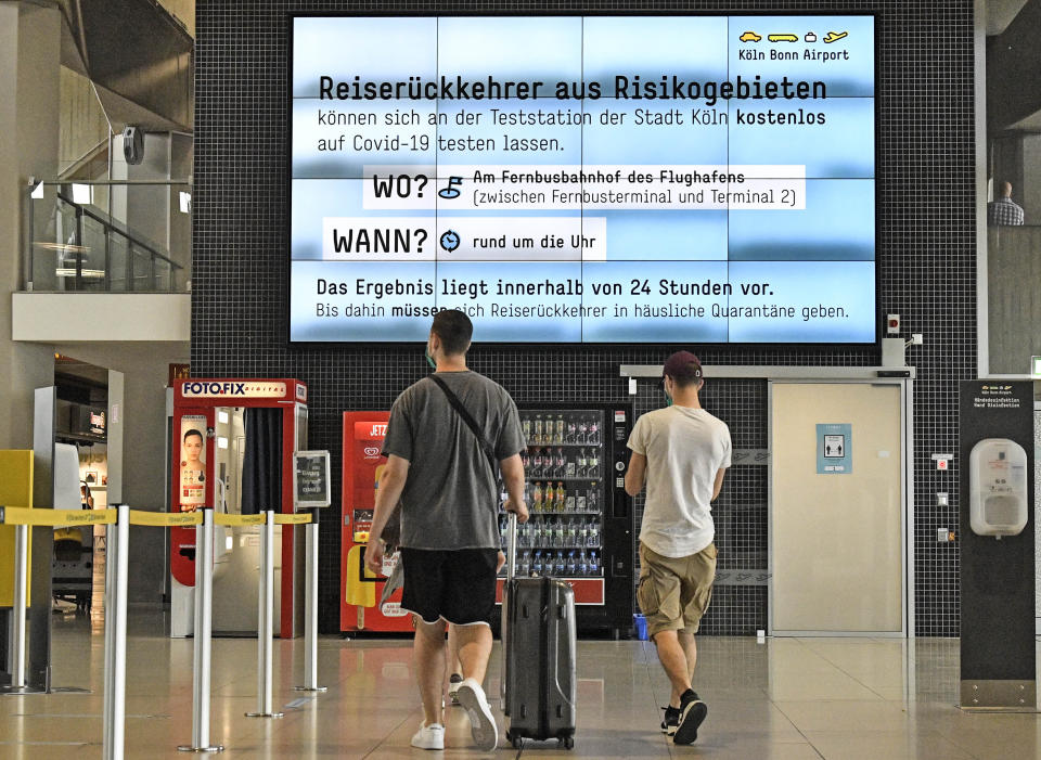 Travellers walk at the airport in front of a board reading "Free tests for returnees from countries designated as risk areas" in Cologne, Germany, Tuesday, July 28, 2020. New test centers for coronavirus are established at German airports due to the pandemic and free corona tests are given for returnees from countries designated as risk areas. (AP Photo/Martin Meissner)