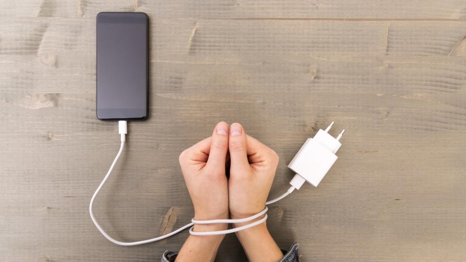 Foto de una manos amarradas al cable de un teléfono.