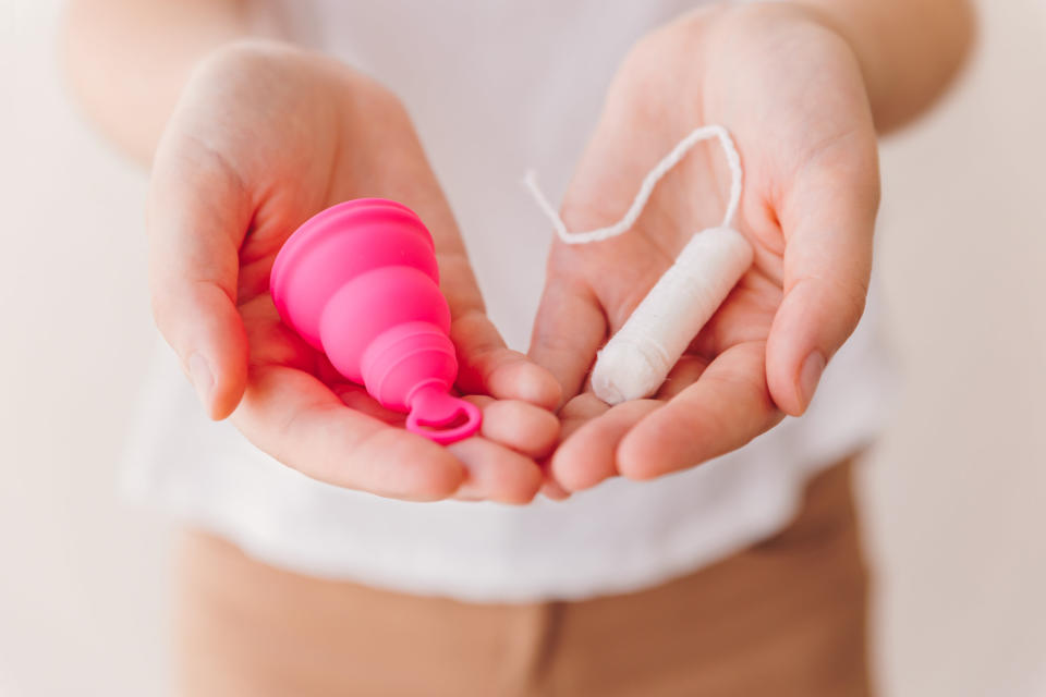 woman holding a menstrual cup in one hand and a tampon in the other