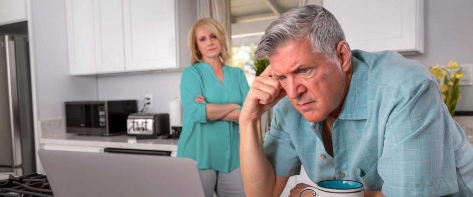 Senior couple in kitchen, looking at laptop and looking stressed