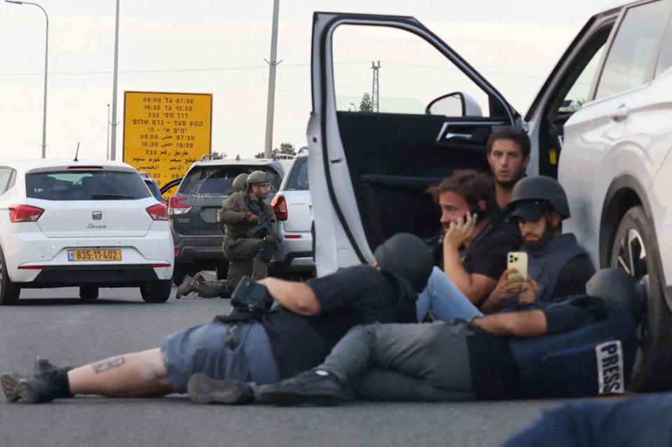 Journalists take cover behind cars as Israeli soldiers take position during clashes with Hamas fighters near the Gevim kibbutz, close to the border with Gaza on October 7, 2023. / Credit: Oren Ziv/AFP via Getty Images