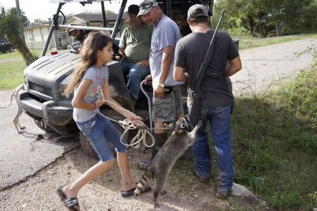 Fernando Rivera Jr. (C) looks at a neigbour's pet raccoon jumping up onto his son Fernando Rivera III's rifle (R) as a group of patriots patrolling in a UTV look on outside their home in Brownsville, Texas September 2, 2014. REUTERS/Rick Wilking