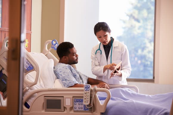 A female doctor talking to a male patient in a hospital bed.