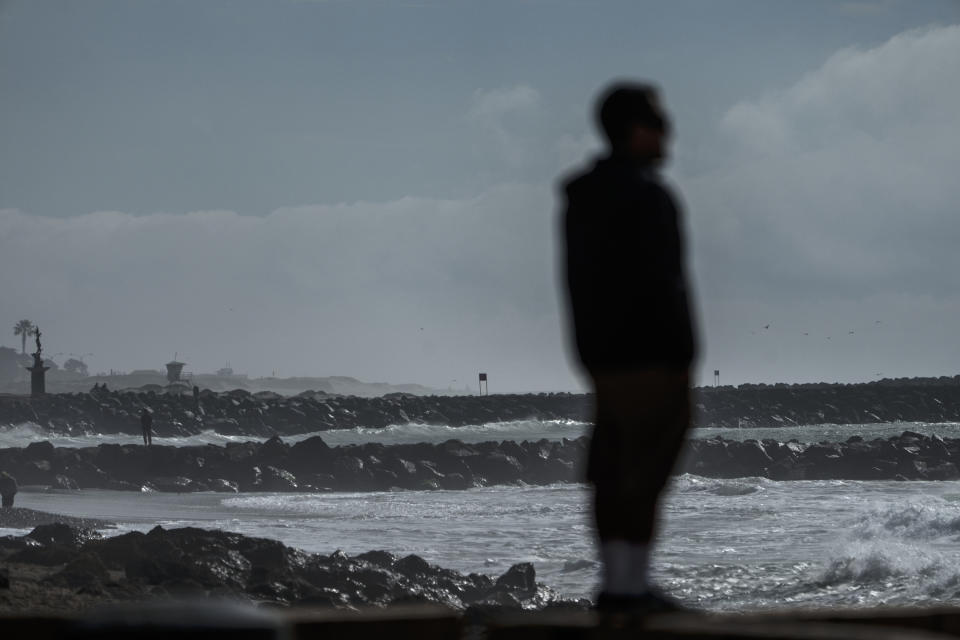 A beach visitor stands on top of a protective sand mound ahead of storms in Ventura, Calif., Wednesday, Jan. 31, 2024. (AP Photo/Damian Dovarganes)