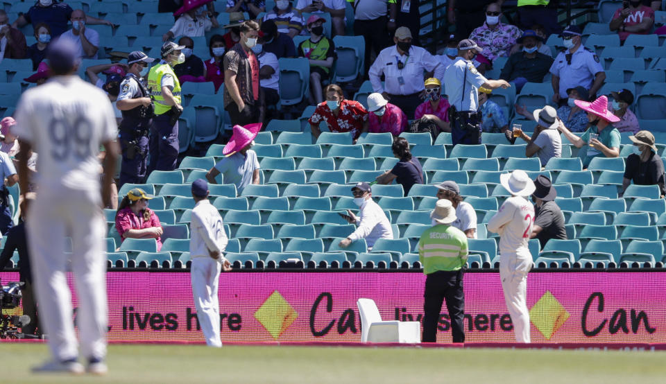 Police, top, remove spectators from the game during play on day four of the third cricket test between India and Australia at the Sydney Cricket Ground, Sydney, Australia, Sunday, Jan. 10, 2021. (AP Photo/Rick Rycroft)