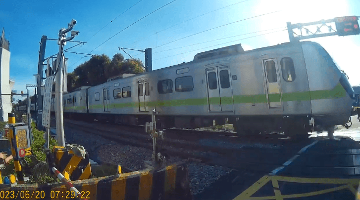 校車車頂碰到柵欄，平交道的列車防護系統因此發出警報，一輛區間快車鳴笛慢行而過。（讀者授權提供）