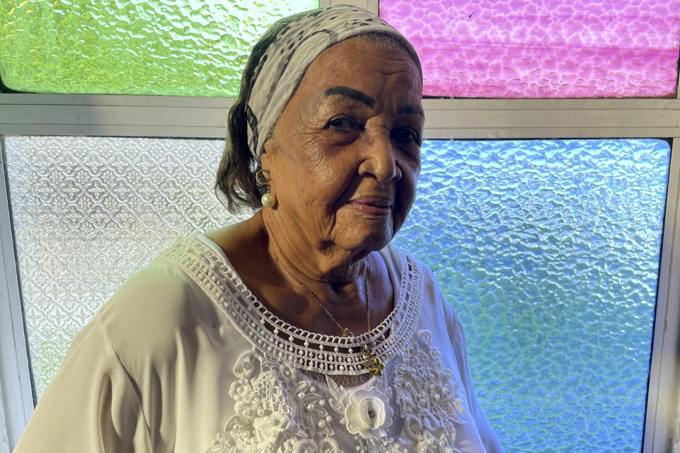 Lucia Barker, 83, a member of the choir at First Baptist Church on Colombia's San Andres Island poses for a portrait in front of stained-glass windows on Thursday, Aug. 18. 2022. "This church is my life," Barker says of the sanctuary where she was baptized, married and has worshipped for more than seven decades. (AP Photo/Luis Andres Henao)