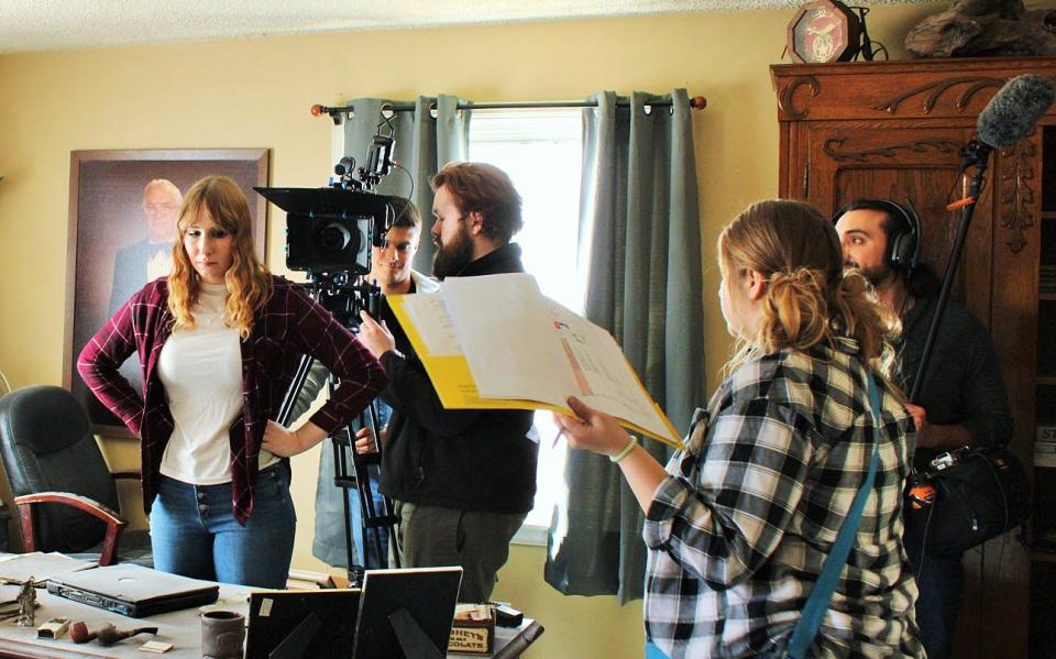A Cintree Films crew prepares to shoot a scene for their short film titled “Shut the Box” staged in a house in Newhall, Iowa. ISU theatre major Caitlin Allen has the principal role and stands before the desk, while Michael Huntington adjusts a camera and Brittany Benedict directs the action.