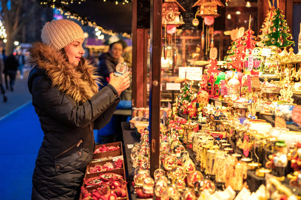 A woman looking at a snow-globe as she browses a stall of traditional Christmas decorations and toys at a market stall in Edinburgh, Scotland.