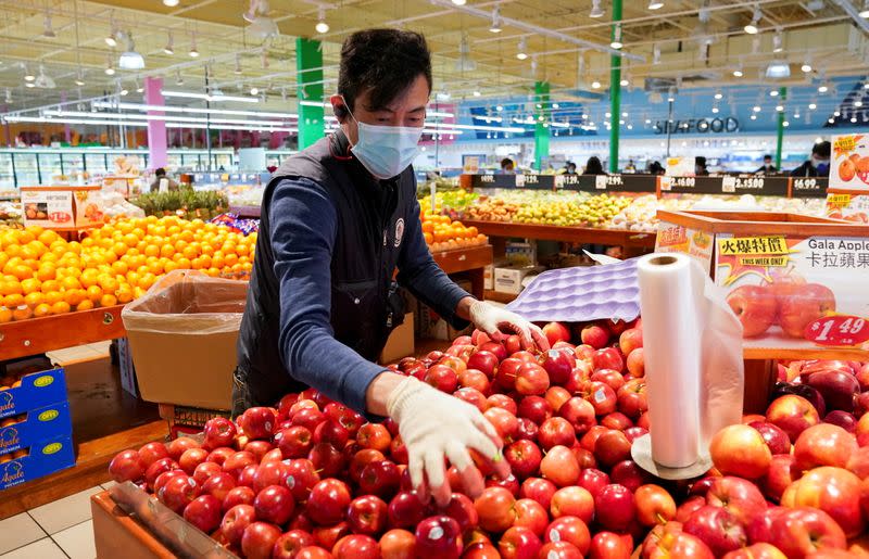 FILE PHOTO: Wearing a mask and gloves, a worker re-stocks apples in a Asian grocery store in Falls Church, Virginia