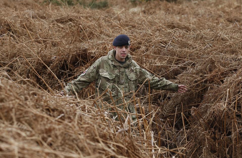A British army officer walks on a WW1 practise trench as he poses for the photographers in Gosport, southern England, Thursday, March 6, 2014. This overgrown and oddly corrugated patch of heathland on England’s south coast was once a practice battlefield, complete with trenches, weapons and barbed wire. Thousands of troops trained here to take on the Germany army. After the 1918 victory _ which cost 1 million Britons their lives _ the site was forgotten, until it was recently rediscovered by a local official with an interest in military history. Now the trenches are being used to reveal how the Great War transformed Britain _ physically as well as socially. As living memories of the conflict fade, historians hope these physical traces can help preserve the story of the war for future generations. (AP Photo/Lefteris Pitarakis)