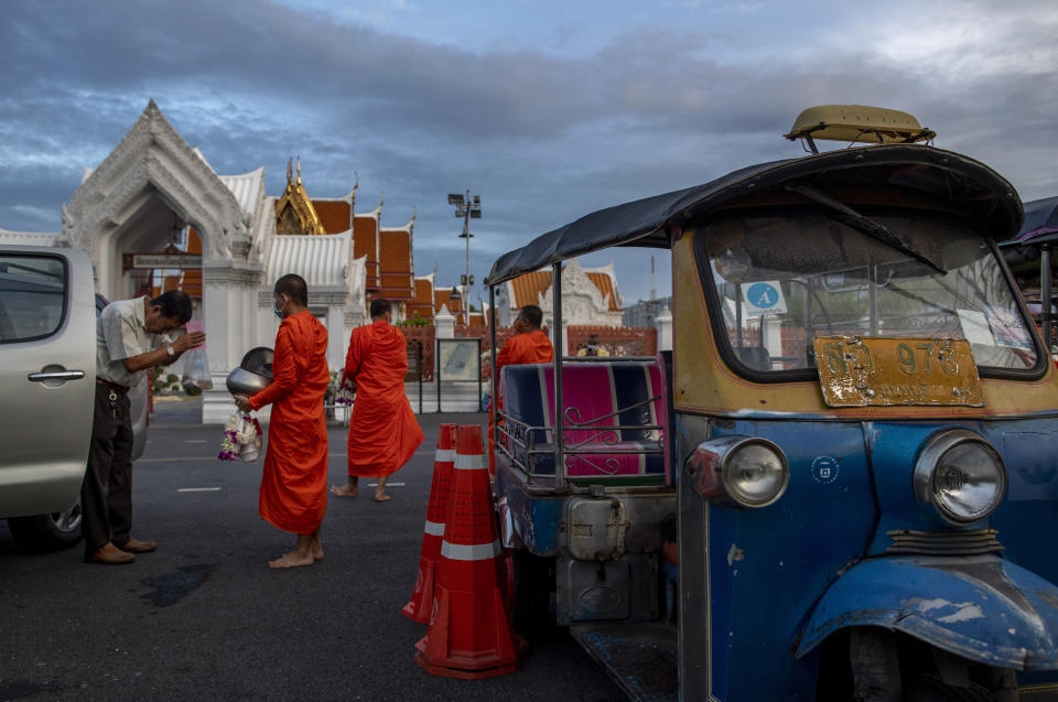 A man offers alms to monks outside the temple of the Emerald Buddha at dawn in Bangkok, Thailand, Wednesday, May 27, 2020. Thai government continues to ease restrictions related to running business in capital Bangkok that were imposed weeks ago to combat the spread of COVID-19. (AP Photo/ Gemunu Amarasinghe)