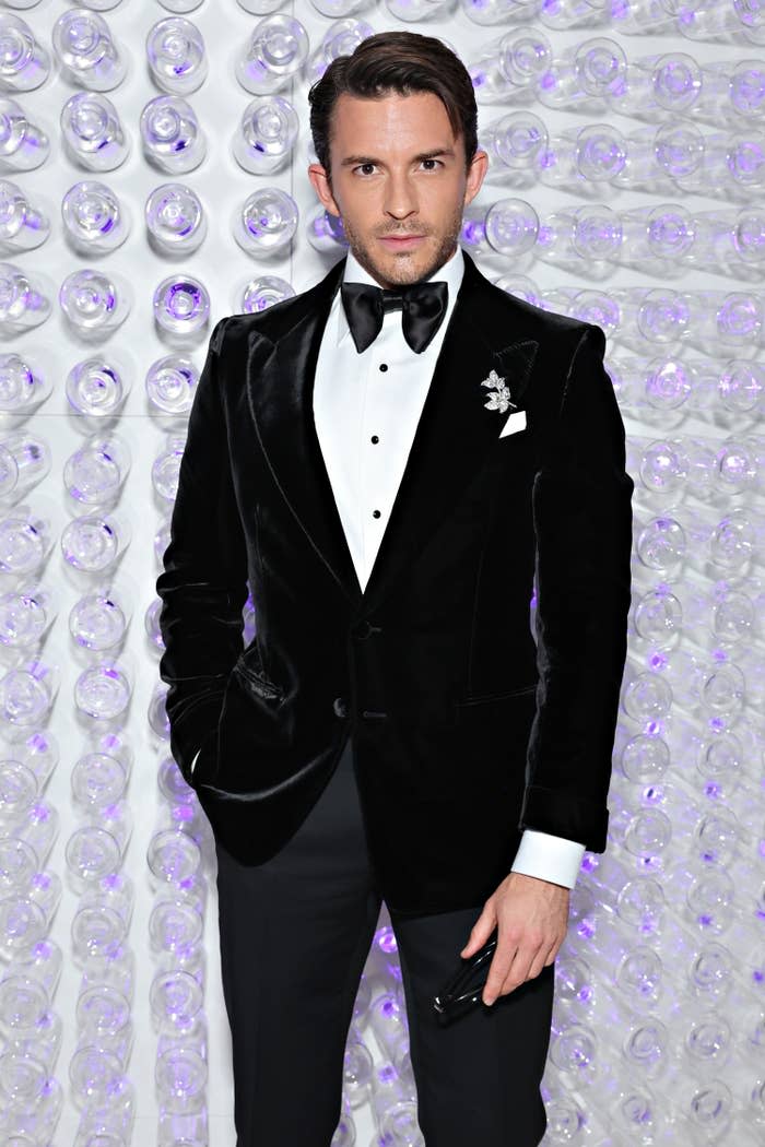 jonathan bailey poses on red carpet in a tuxedo with a velvet jacket