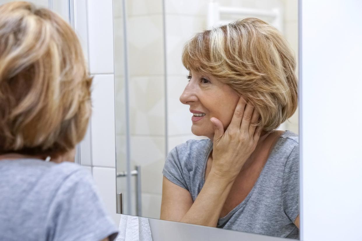 middle-aged woman examining her face in the mirror