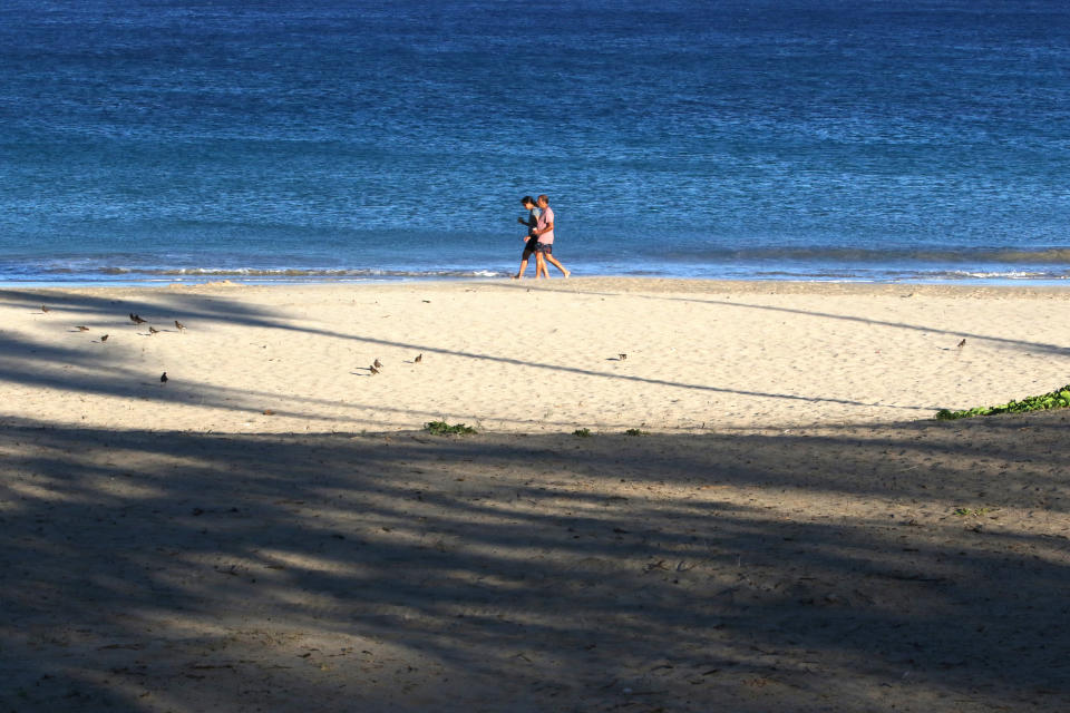 A couple walks on a beach near Waimea, Hawaii, on Friday, Aug. 6, 2021. The area was scorched by the state's largest ever wildfire. Wildfires in the Pacific Islands are becoming more common as drought conditions increase along with climate change. Fires on many islands in the Pacific burn a proportion of land equal to fires in U.S. Western states and the blazes are causing a cascading effect of environmental damage that impacts island communities that rely on the local ecosystems. (AP Photo/Caleb Jones)