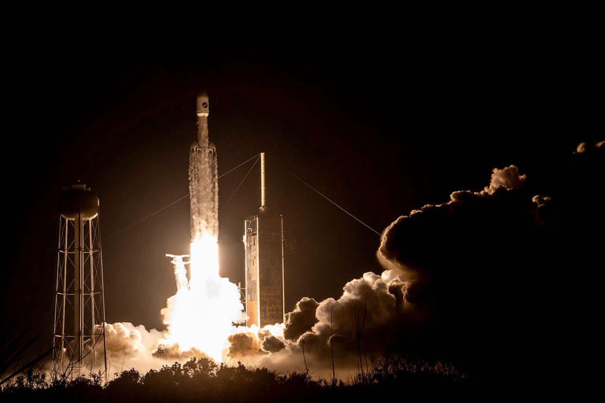  A white rocket with three boosters launching at night. 