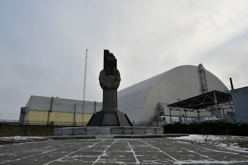 (FILES) This file photograph taken on December 8, 2020 shows a monument in front of the giant protective dome built over the sarcophagus of the destroyed fourth reactor of Chernobyl nuclear power plant. Ukraine's Chernobyl nuclear plant says 'completely halted' over Russian offensive. / AFP / GENYA SAVILOV